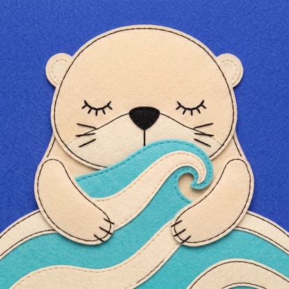 NaniNani’s mark: a felt otter with closed eyes, hugging a wave-shaped pillow